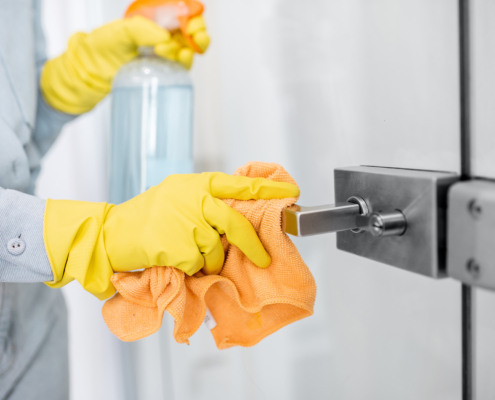 Woman in protective gloves disinfecting door handle while cleaning